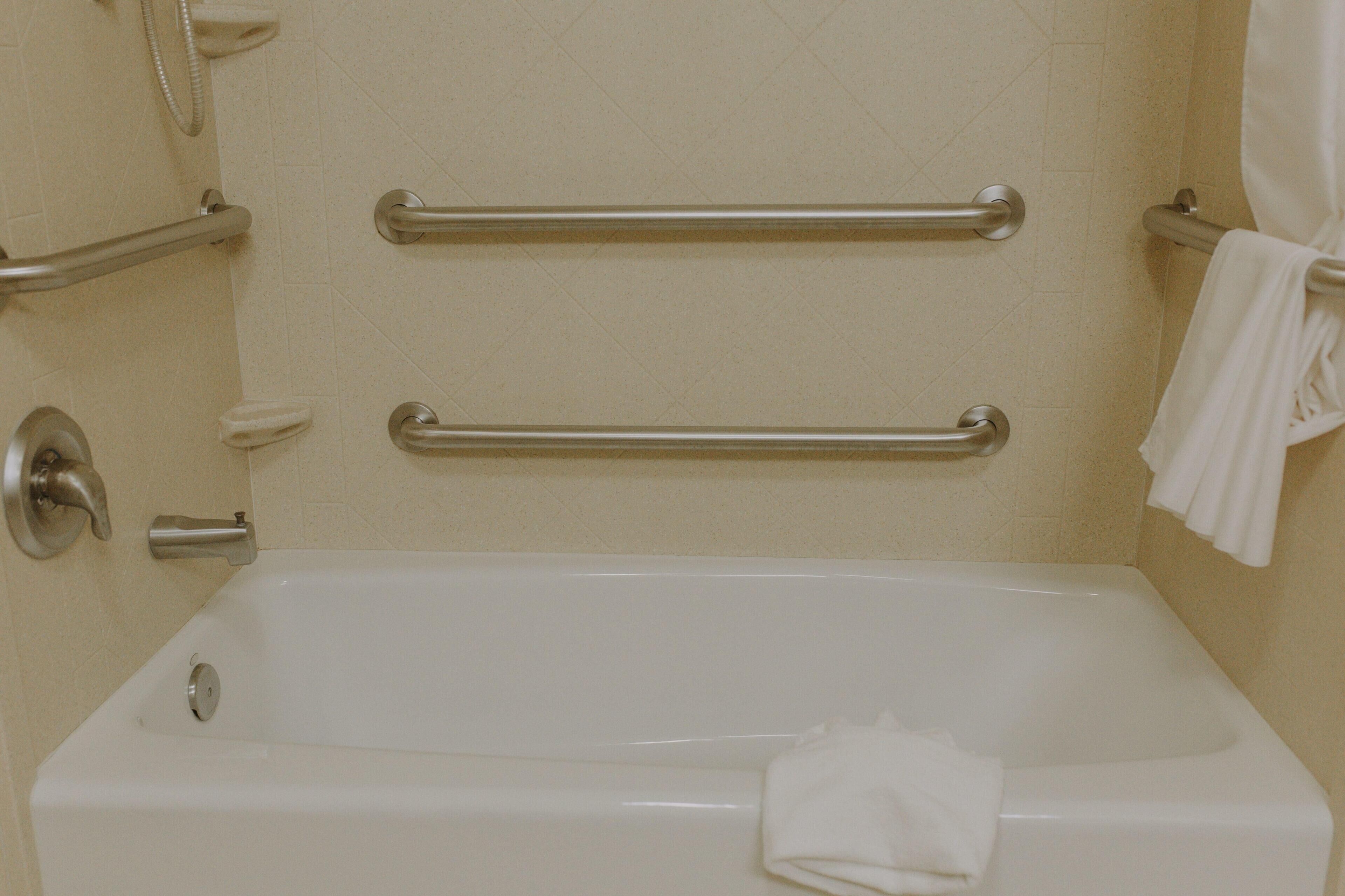 A white bathtub with two metal grab bars, a faucet, and a towel hanging on the wall.