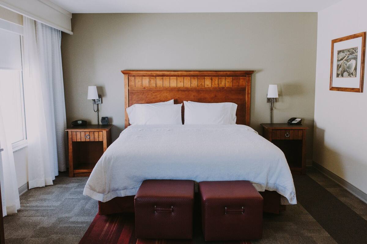 Une chambre d’hôtel avec un grand lit, deux tables de chevet, une tête de lit en bois et un tableau encadré au mur.