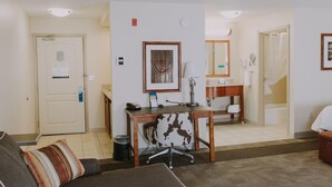 Habitación de hotel con sofá, escritorio, espejo, baño con ducha y puerta con un cartel.