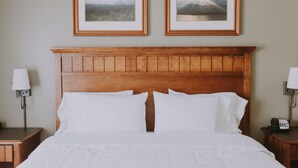 Una cama bien hecha con sábanas blancas, un cabecero de madera y dos cuadros en la pared de arriba.