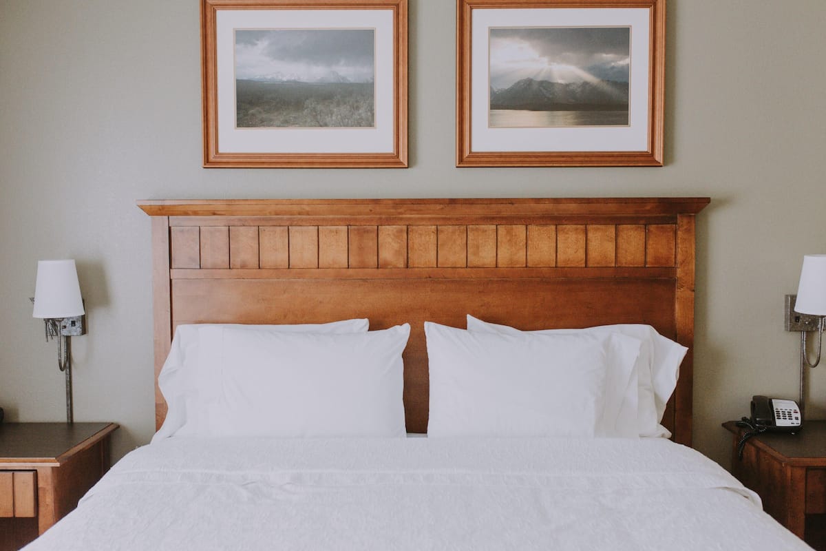 Un lit bien fait, avec du linge de lit blanc, une tête de lit en bois et deux tableaux encadrés accrochés au mur au-dessus.
