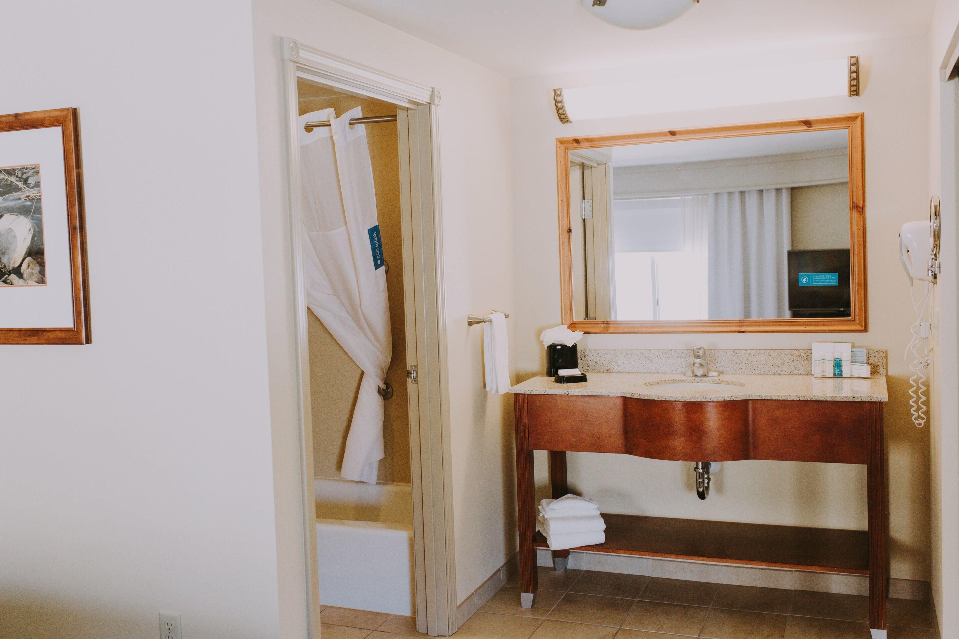 A bathroom with a wooden vanity, a large mirror, a shower curtain, and a towel rack.
