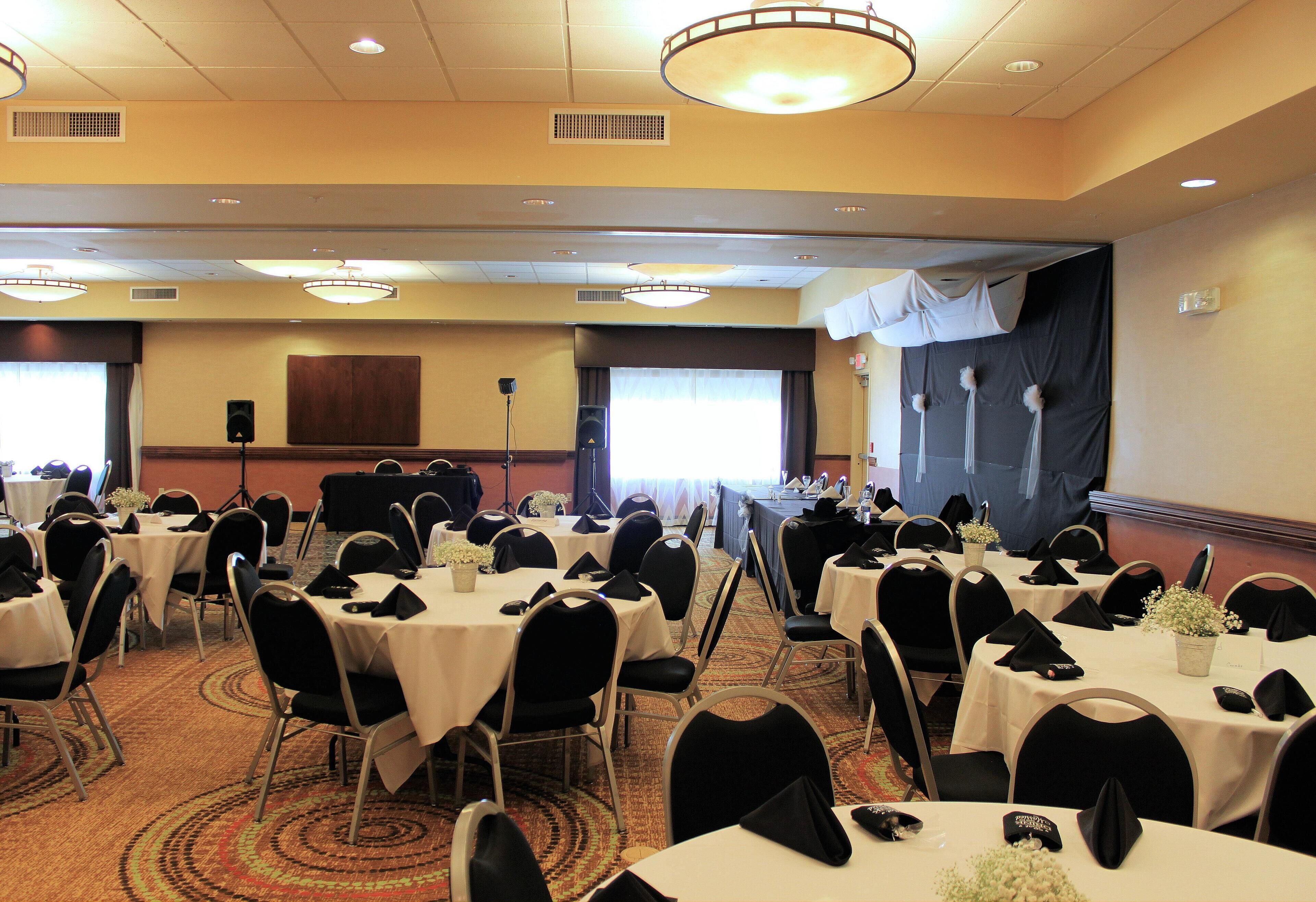 A conference room with multiple round tables, black chairs, and white tablecloths.
