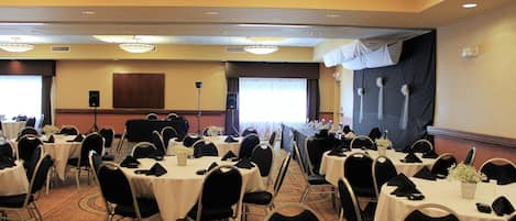 A conference room with multiple round tables, black chairs, and white tablecloths.