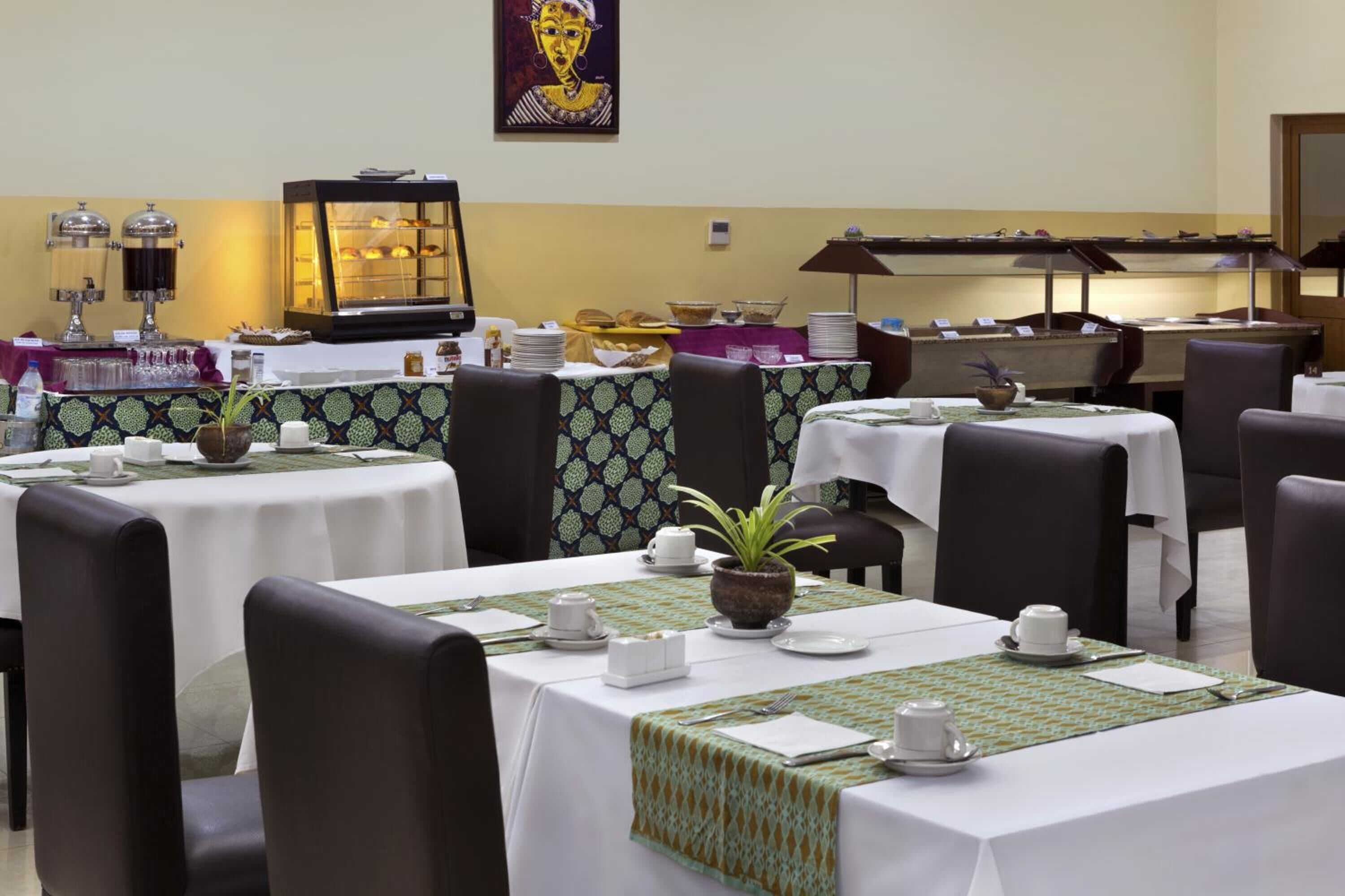 Un espace repas avec des tables préparées pour le petit-déjeuner, comprenant un buffet proposant divers plats et un coin café.