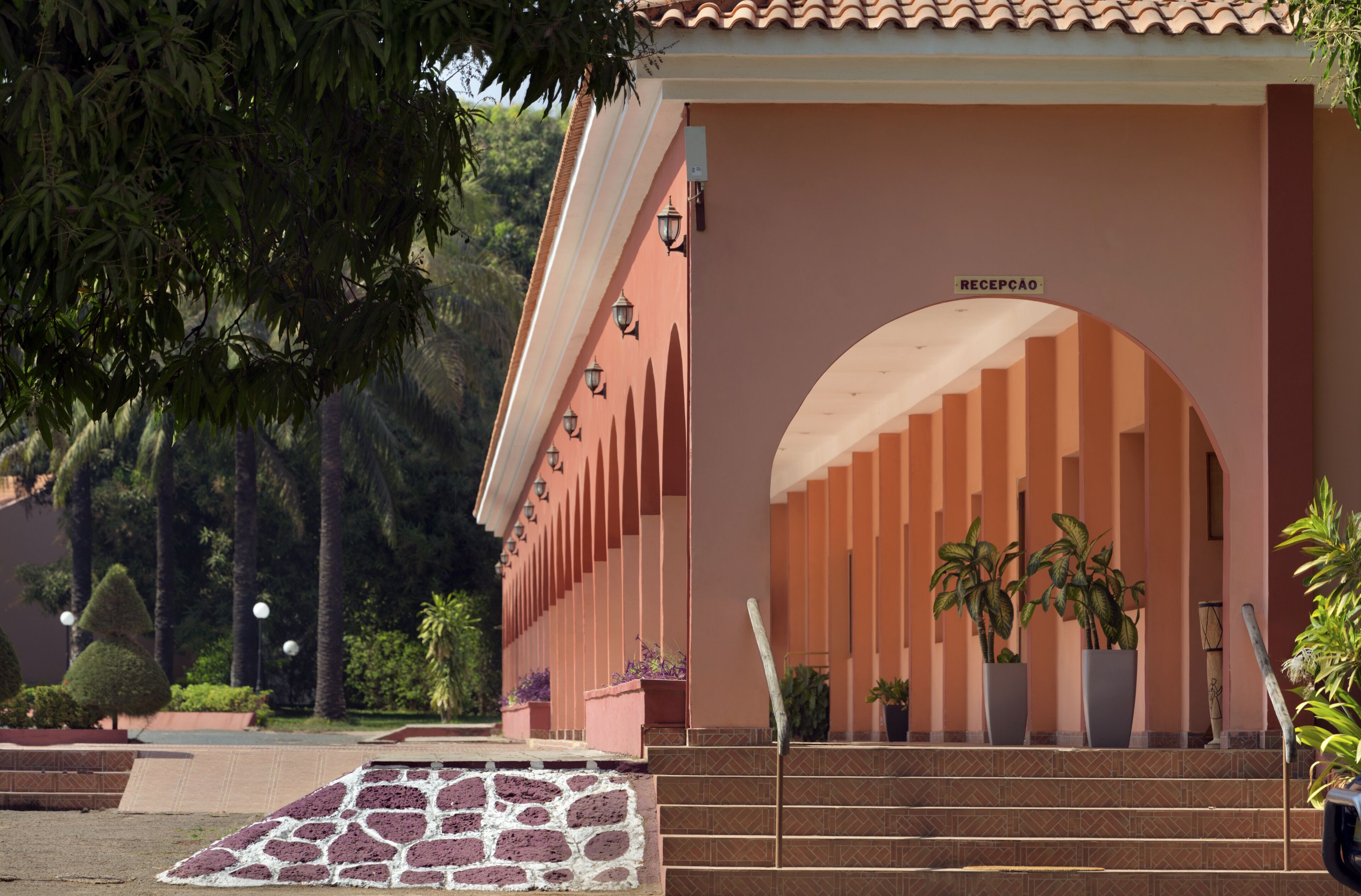 A building entrance with a sign reading "RECEPCAO," steps leading up to it, and potted plants.