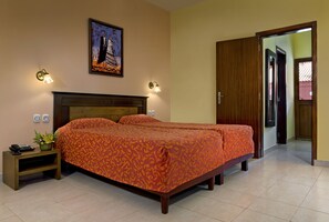 Een tweepersoonsbed met een oranje beddekleed, een nachtkastje met een telefoon en een plant, en een schilderij aan de muur.