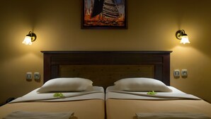 Een hotelkamer met twee bedden, een houten hoofdbord, wandlampen en een schilderij boven de bedden.