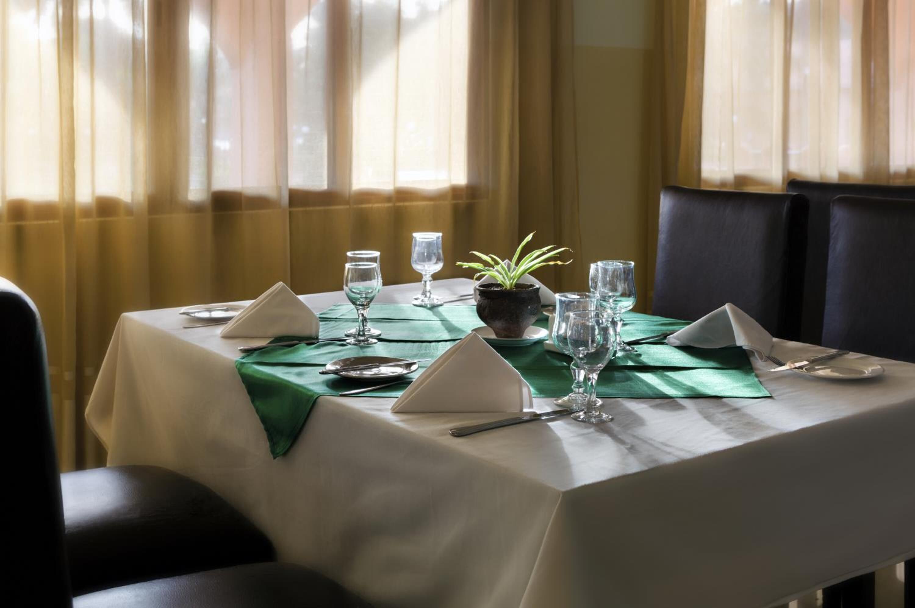 A dining table set with green tablecloths, white napkins, and clear glassware.