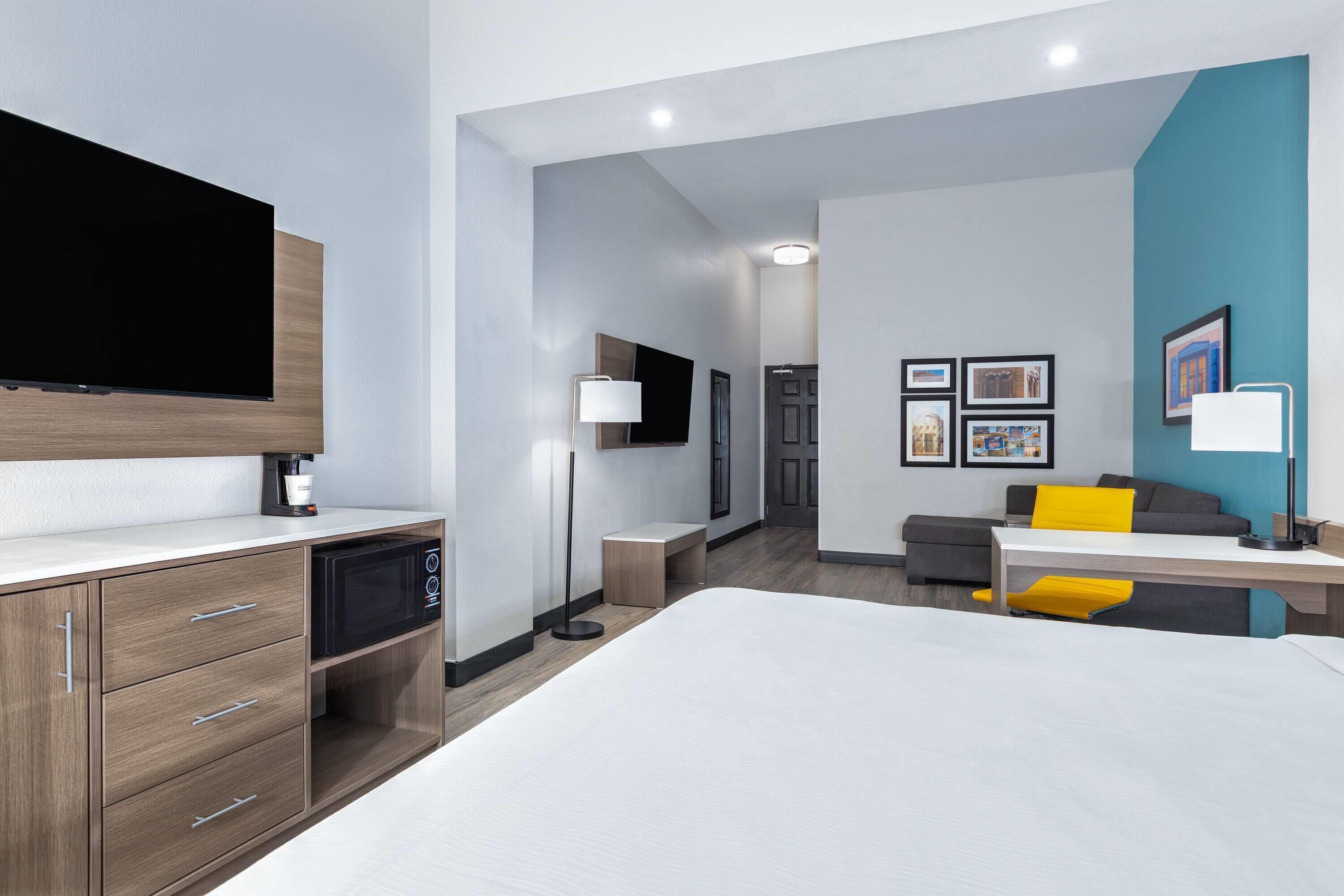 A modern hotel room with a bed, a desk, a flat-screen TV, a microwave, and a seating area with a sofa and armchairs.
