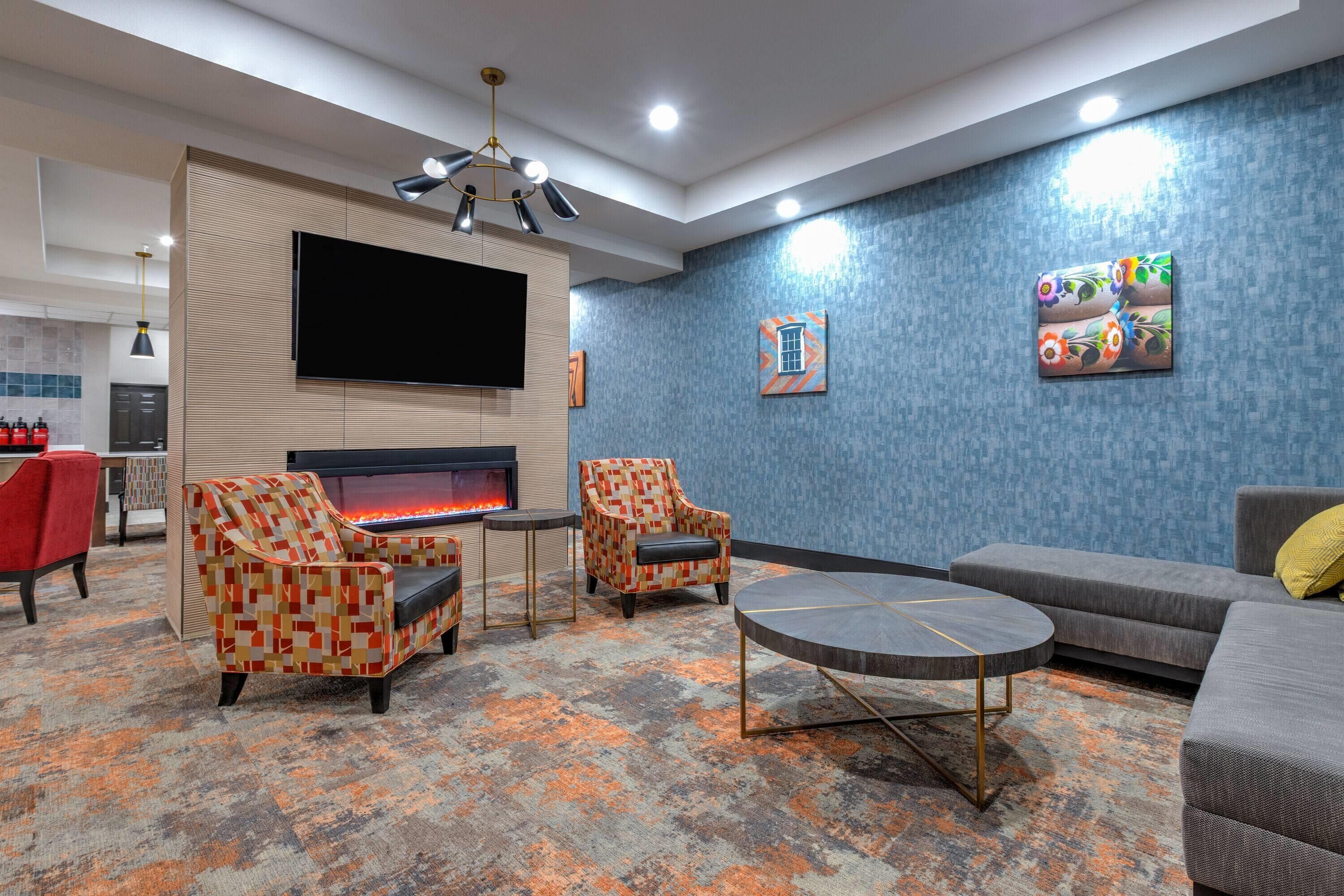 A modern living room with a fireplace, two patterned armchairs, a grey sofa, and a round coffee table.