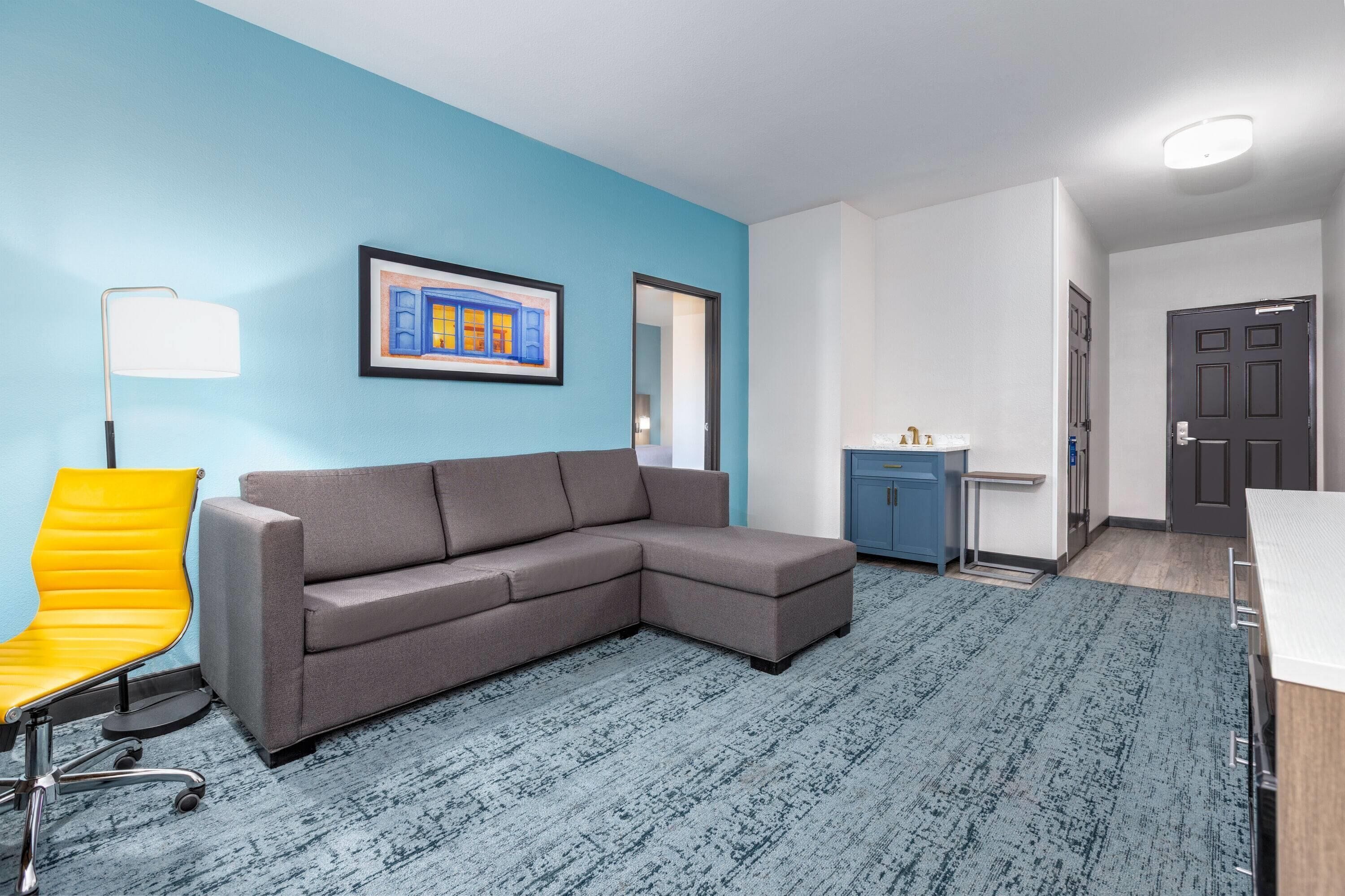 A modern living room with a gray sectional sofa, a yellow chair, and a blue carpet.