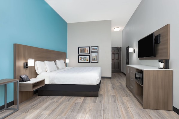 A modern hotel room with a large bed, a desk with a phone, a flat-screen TV, and a kitchenette.