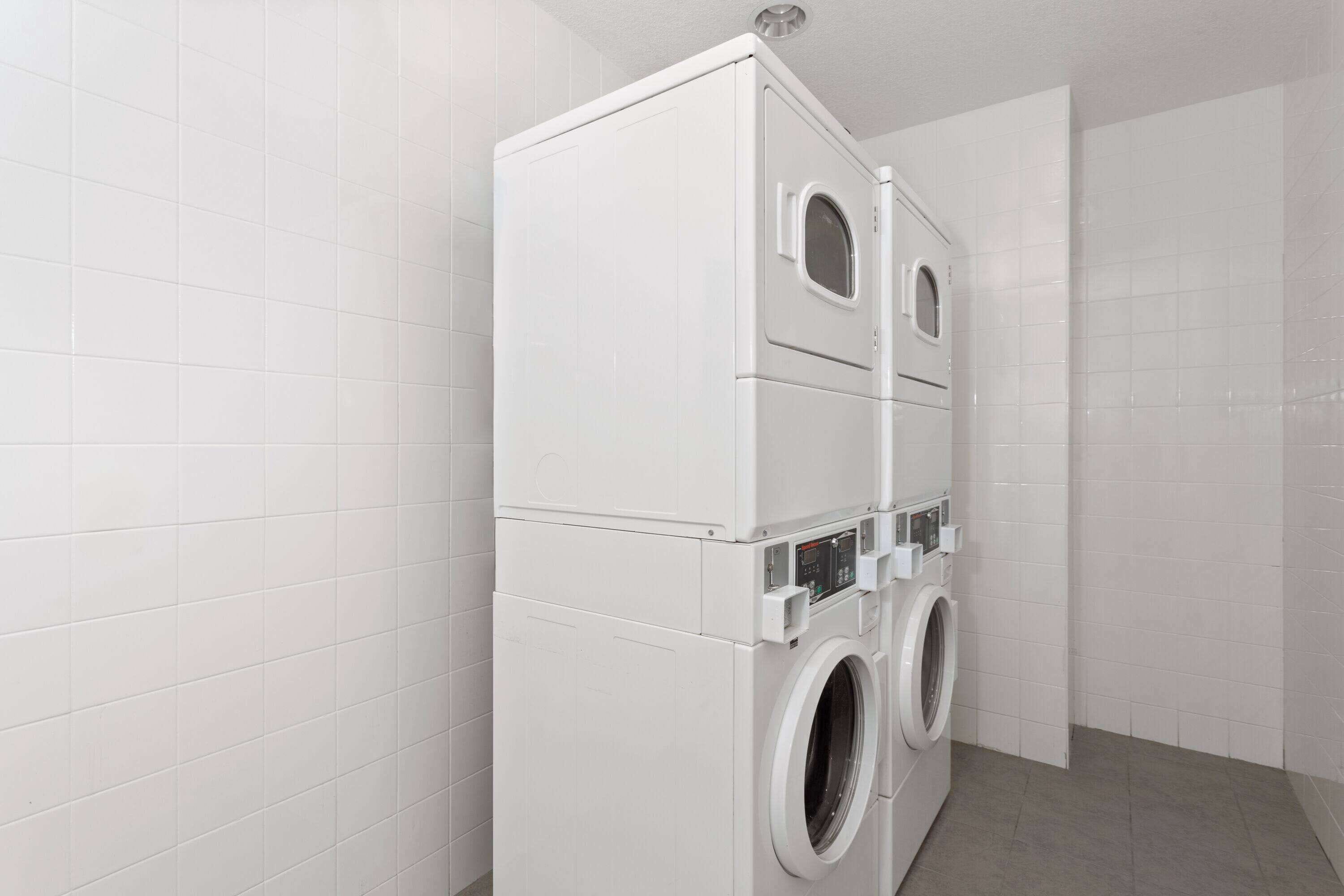 A laundry room with a stacked washer and dryer, white tiled walls, and a grey floor.