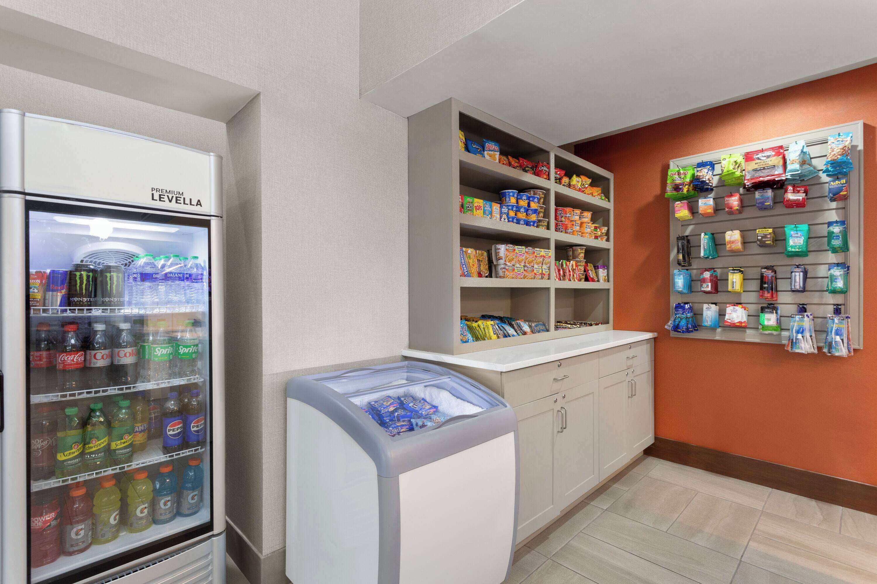 Estação de bebidas de serviço próprio, com frigorífico e congelador, abastecida com diversas bebidas e snacks.