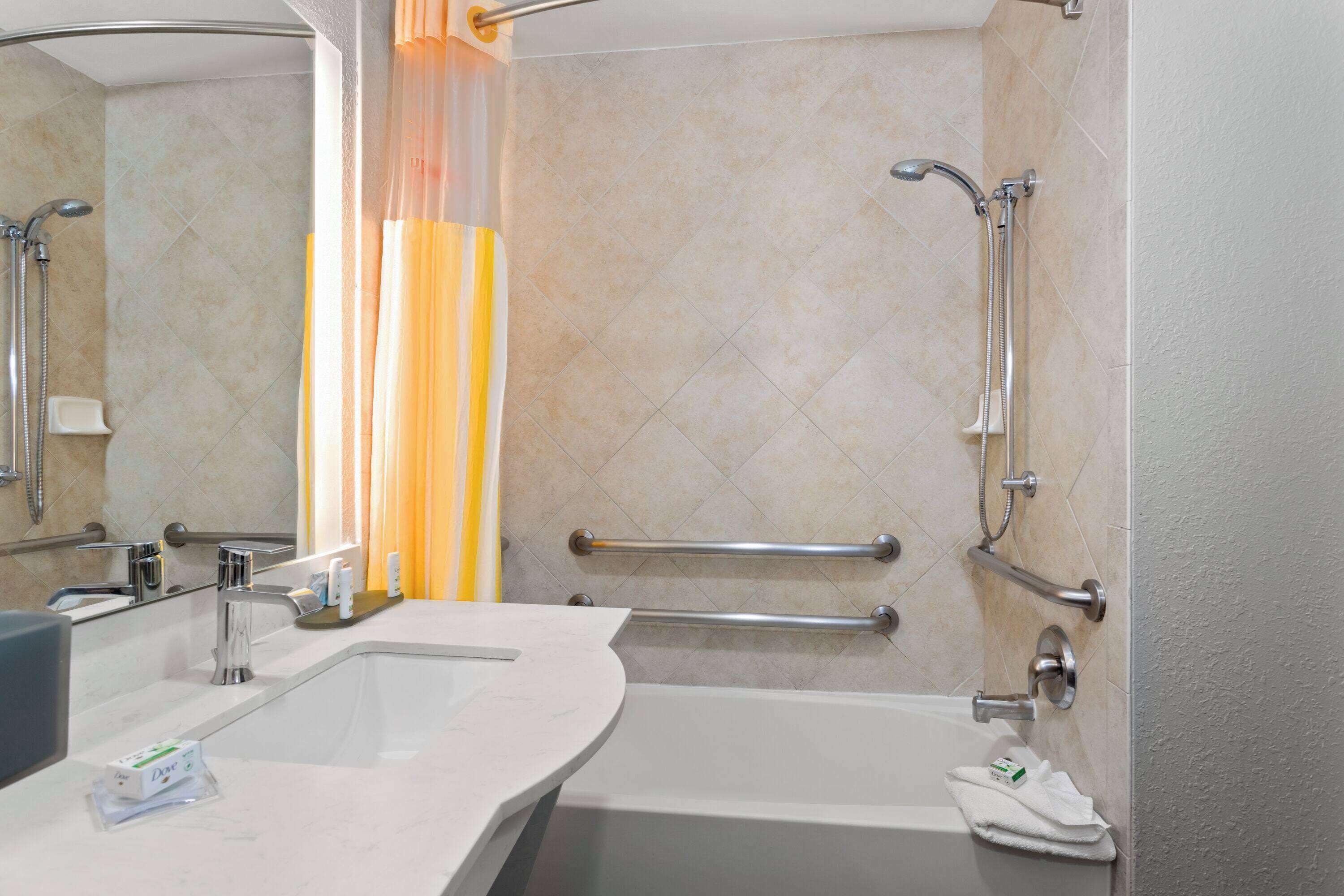 A modern bathroom with a sink, mirror, shower, and grab bars.