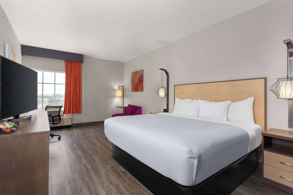 Een hotelkamer met een groot bed, een bureau met een computer, een stoel en een raam met gordijnen.