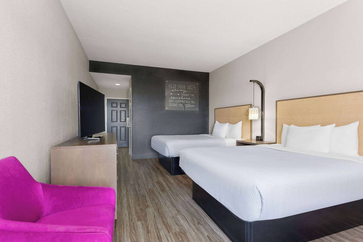 Een hotelkamer met twee bedden, een televisie, een bureau en een felroze stoel.