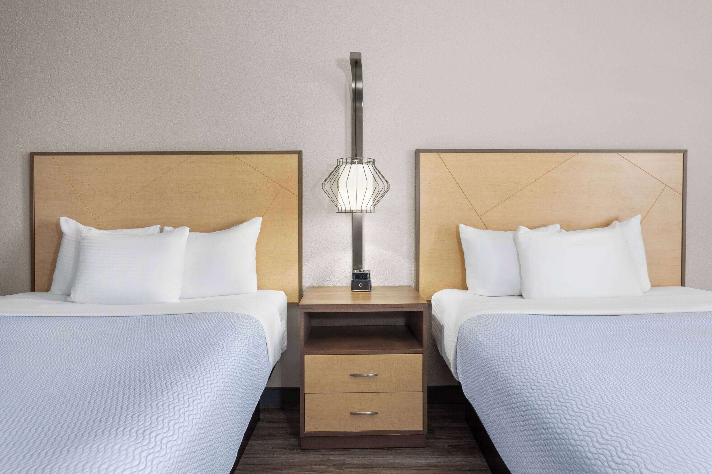 A hotel room with two beds, a nightstand with a lamp, and a wooden headboard.