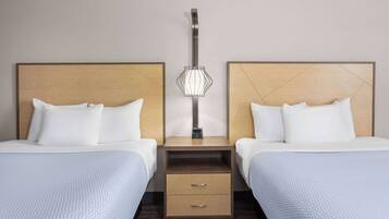 A hotel room with two beds, a nightstand with a lamp, and a wooden headboard.
