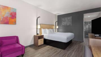 A modern hotel room with a bed, a desk, a chair, a nightstand, and a colorful abstract painting.