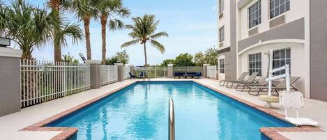 A rectangular swimming pool with a metal safety rail in the foreground, surrounded by a white fence.