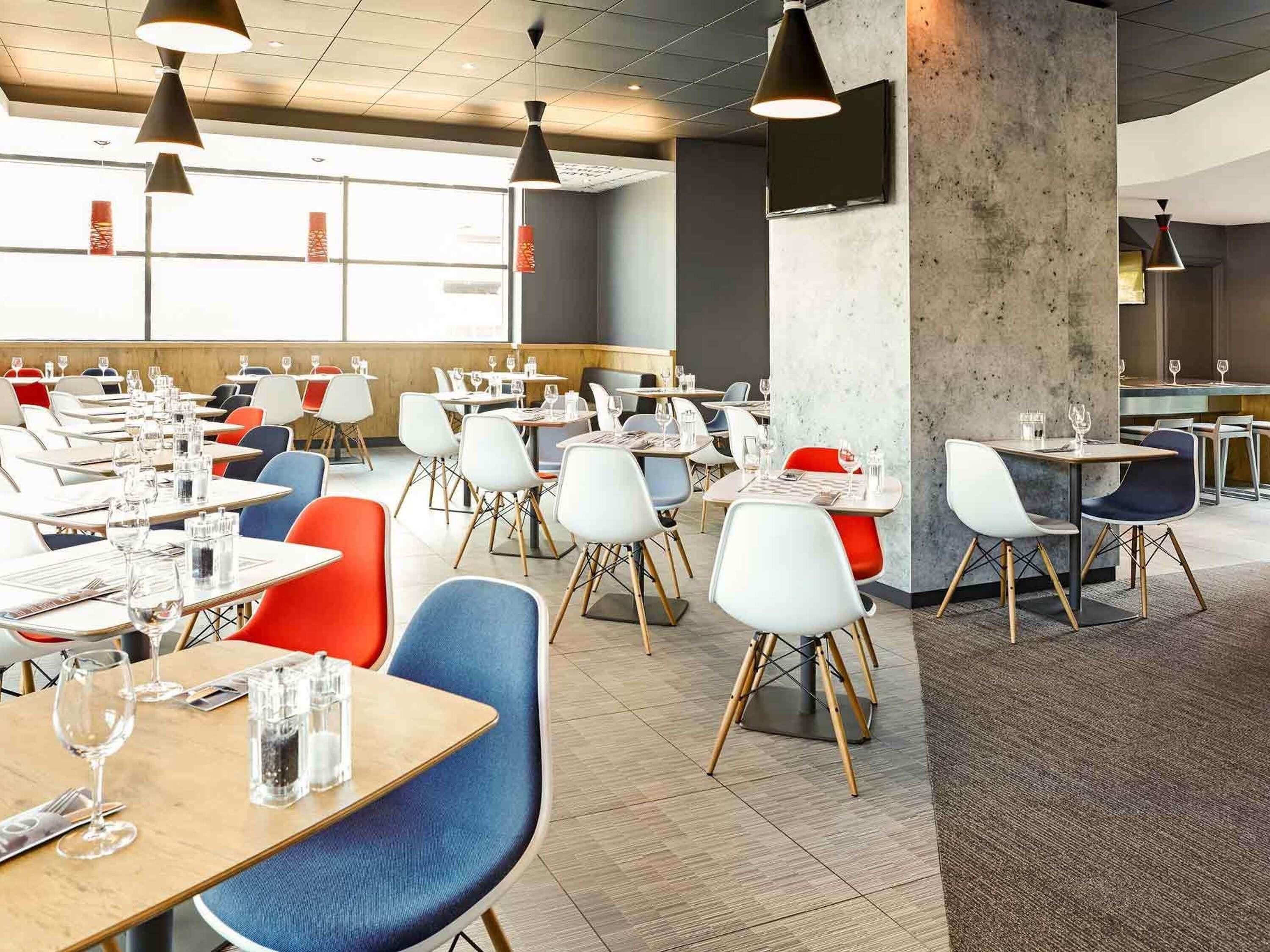 A spacious dining area with multiple tables and chairs, a concrete pillar, and pendant lighting.