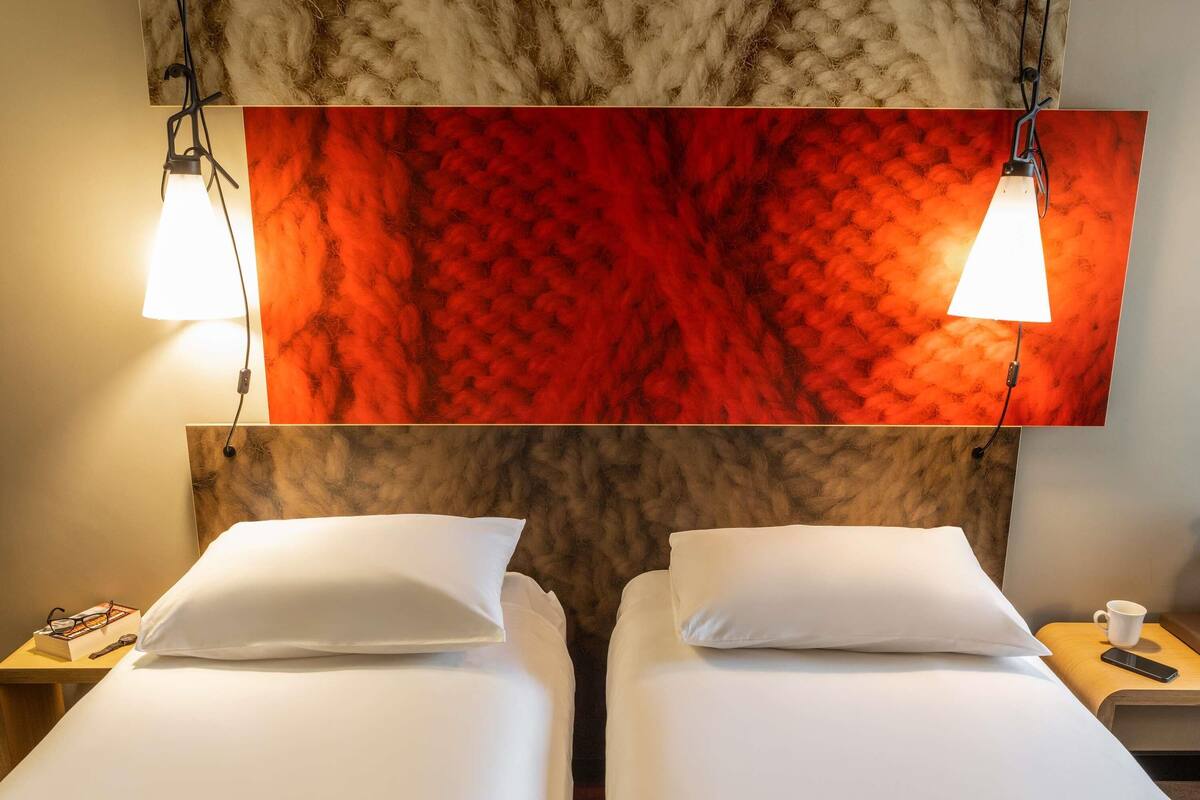 Habitación de hotel con dos camas, una pared texturizada de color rojo y dos lámparas de noche.
