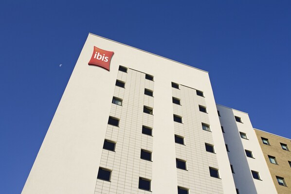 Un edificio moderno con un llamativo letrero de 'ibis' en la fachada, que presenta una cuadrícula de ventanas y un exterior limpio y blanco.