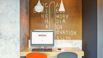 A workspace with a computer, two chairs, a corkboard with words, and pendant lights.