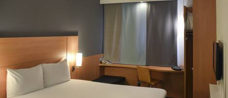 A hotel room with a large bed, bedside lamps, a desk, and a chair.