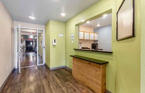 A hallway with a wooden floor, a green wall, and a kitchen area with cabinets and a countertop. - Extended Stay America Select Suites - Phoenix - Peoria - Sun City (Peoria)