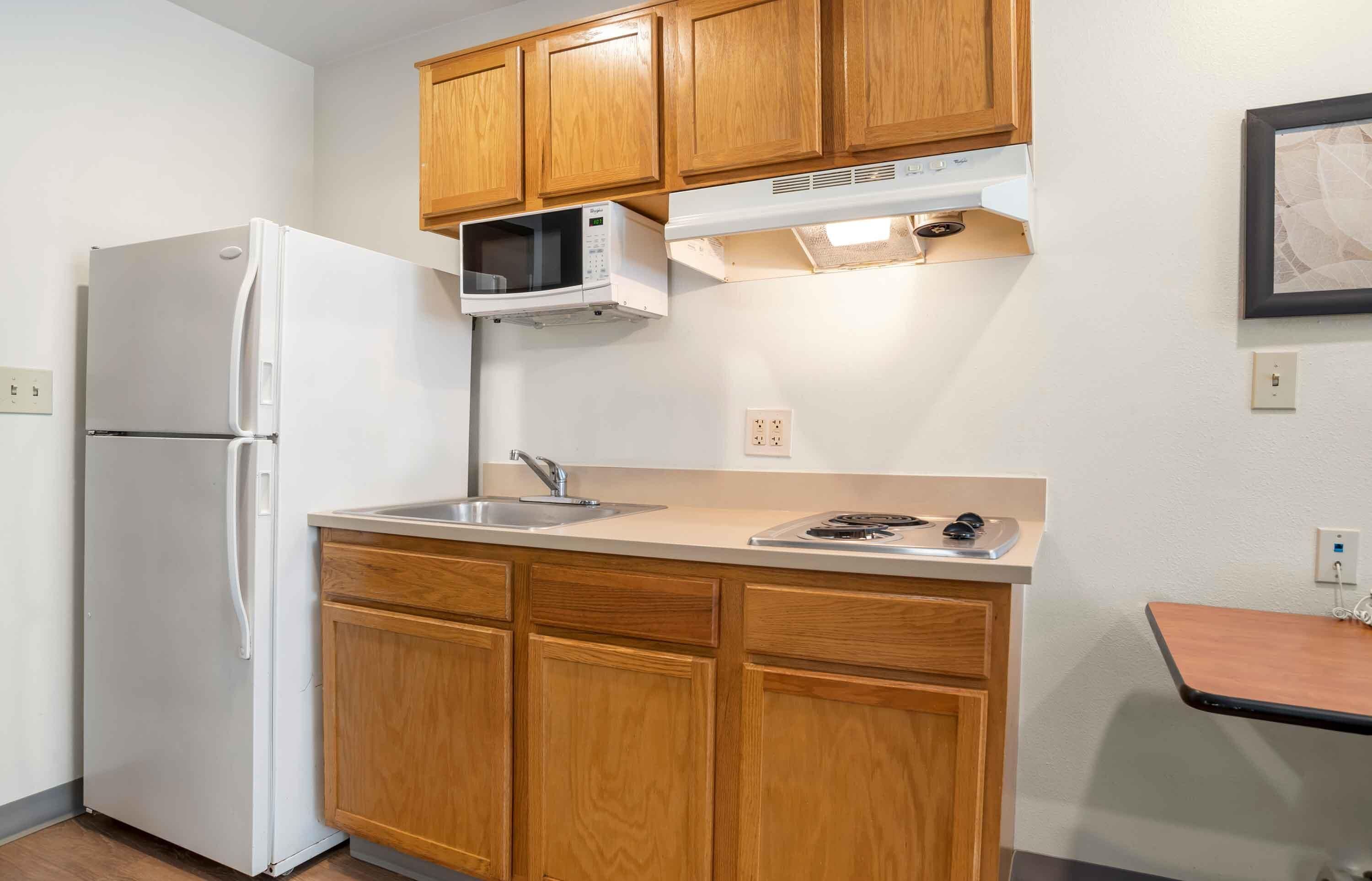 A compact kitchen with wooden cabinets, a white refrigerator, a microwave, a sink, and a small countertop with a stove.