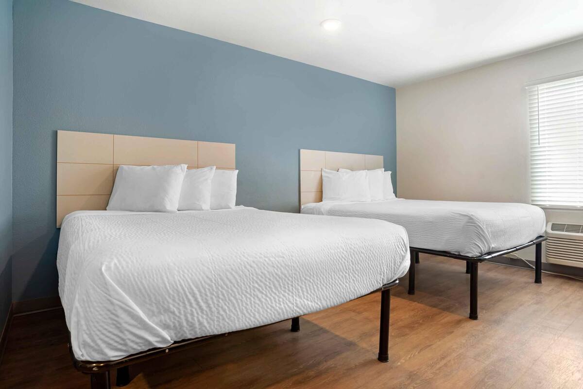 Une chambre d’hôtel avec deux lits, un plancher en bois et une fenêtre avec des stores.