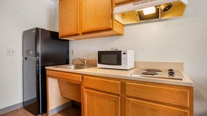 A compact kitchen with wooden cabinets, a black refrigerator, a microwave, and a gas stove. - Extended Stay America Select Suites - Phoenix - Peoria - Sun City (Peoria)