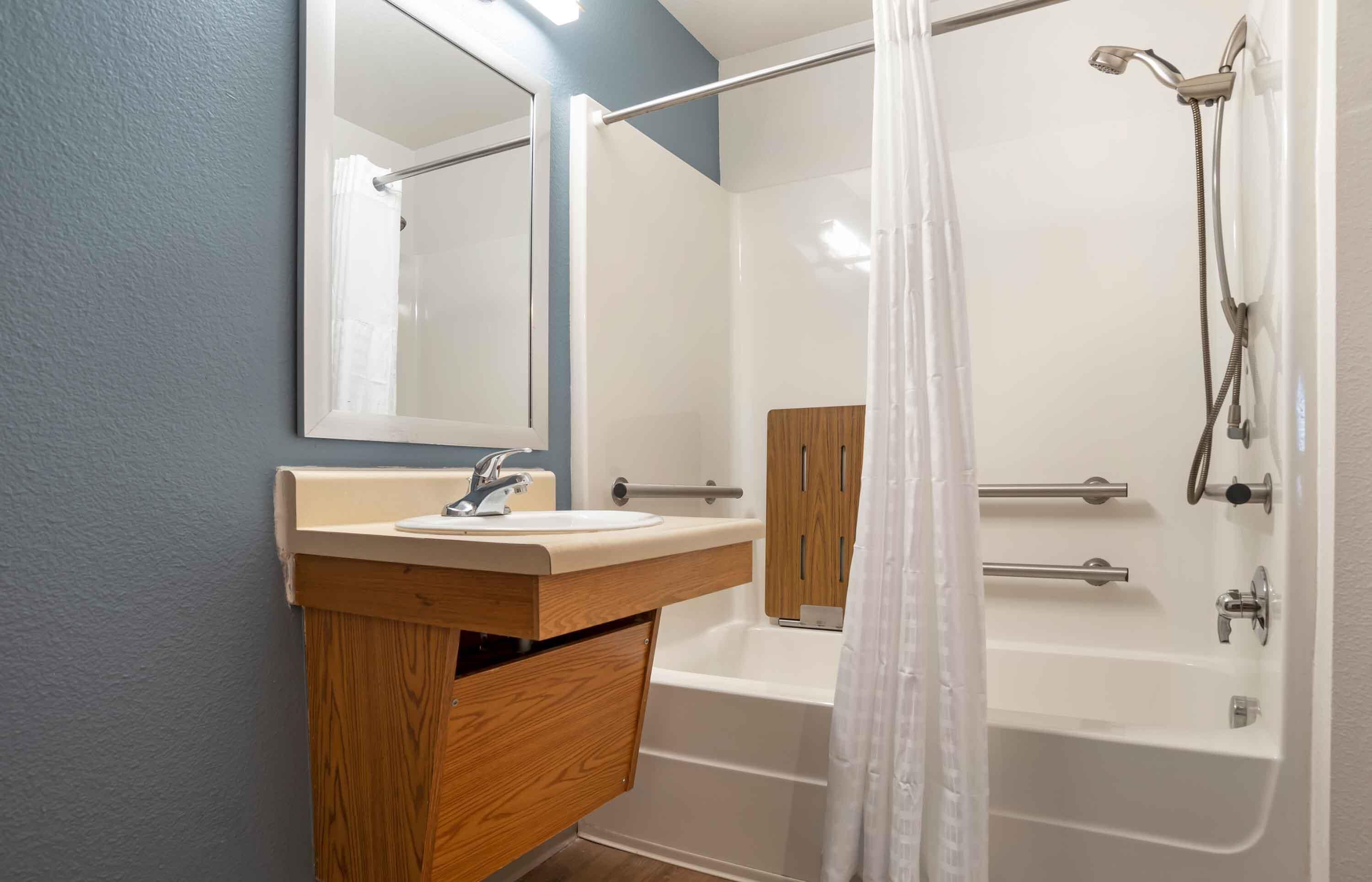 A bathroom with a wooden vanity, a large mirror, a bathtub, and a shower.