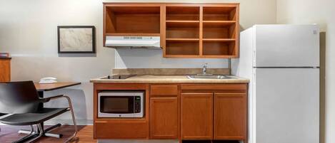 Une cuisine compacte avec des meubles en bois, un four à micro-ondes encastré, un réfrigérateur blanc et un petit coin repas comprenant une chaise et une table.