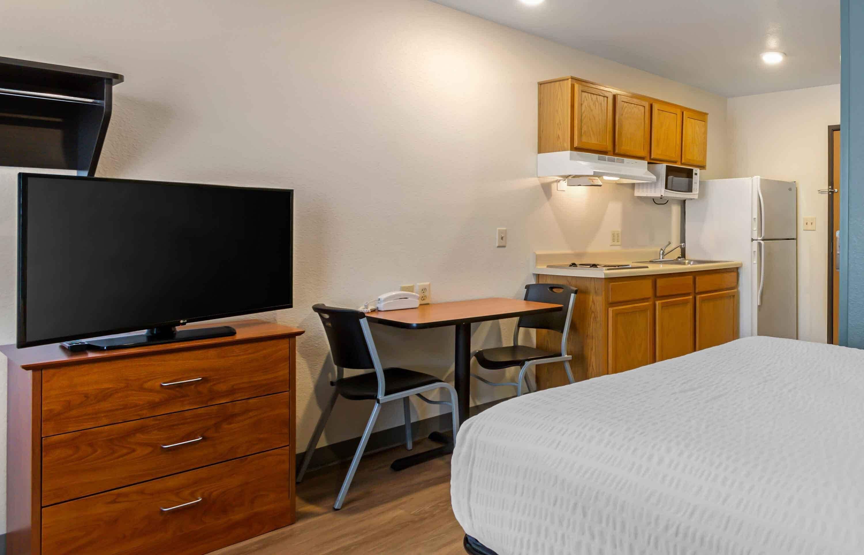Habitación de hotel pequeña con cama, escritorio con silla, televisión, microondas y refrigerador.