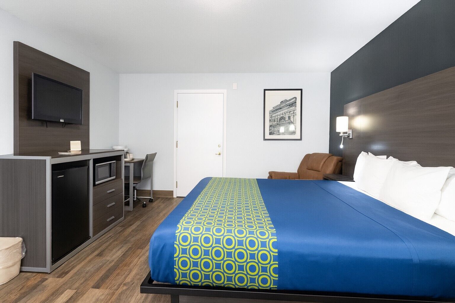 Quarto de hotel com cama, escrivaninha com cadeira, televisão e porta.
