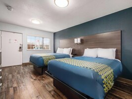 A hotel room with two beds, a wooden floor, a window, and a door.