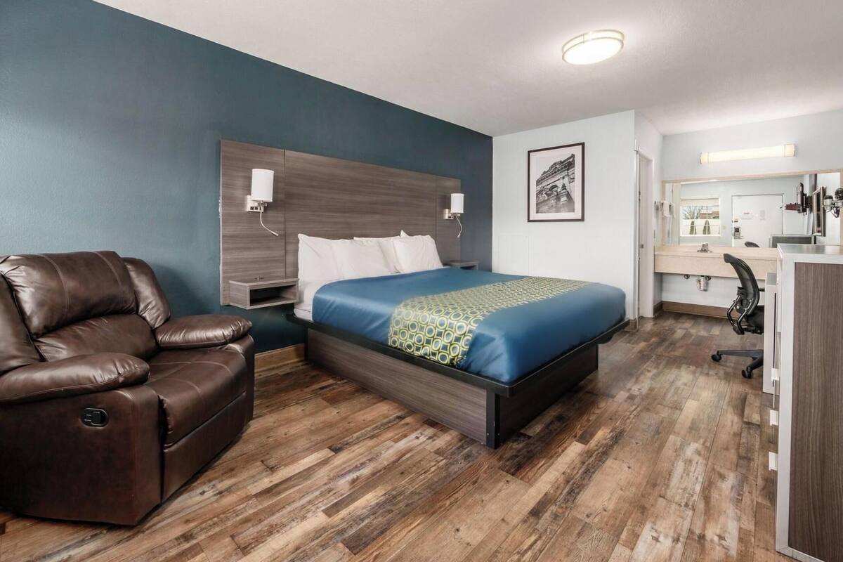 A hotel room with a bed, a leather chair, a desk, and a mirror.