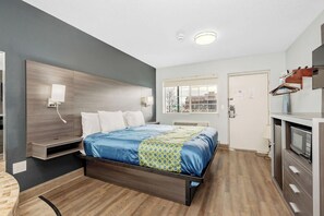 A modern hotel room with a wooden bed, a built-in TV, a kitchenette, and a window with a city view. - Grove City Travel Inn Columbus South (Grove City)
