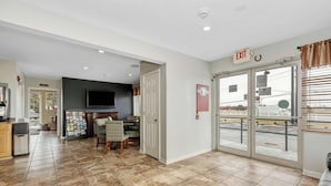 A spacious living area with a dining table, chairs, a flat-screen TV, and a kitchen area with a refrigerator and cabinets.