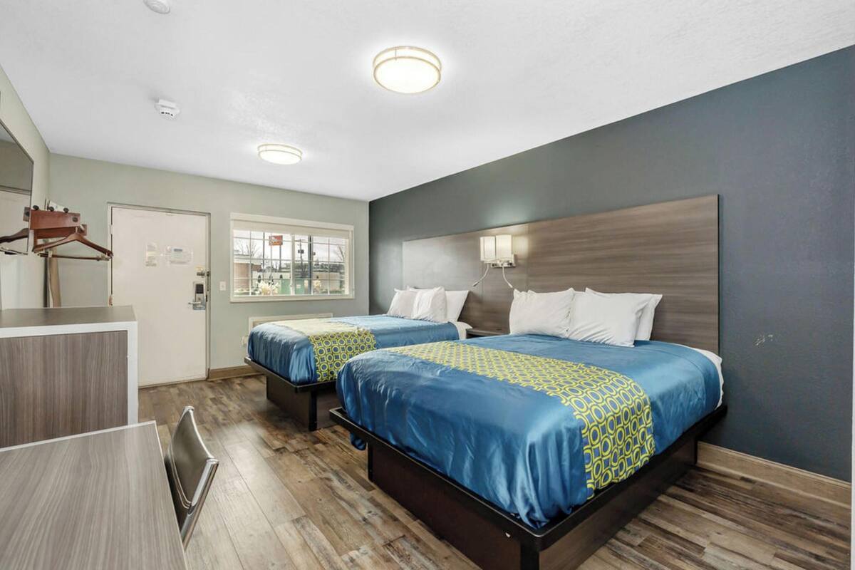 A hotel room with two beds, a desk, and a mirror.