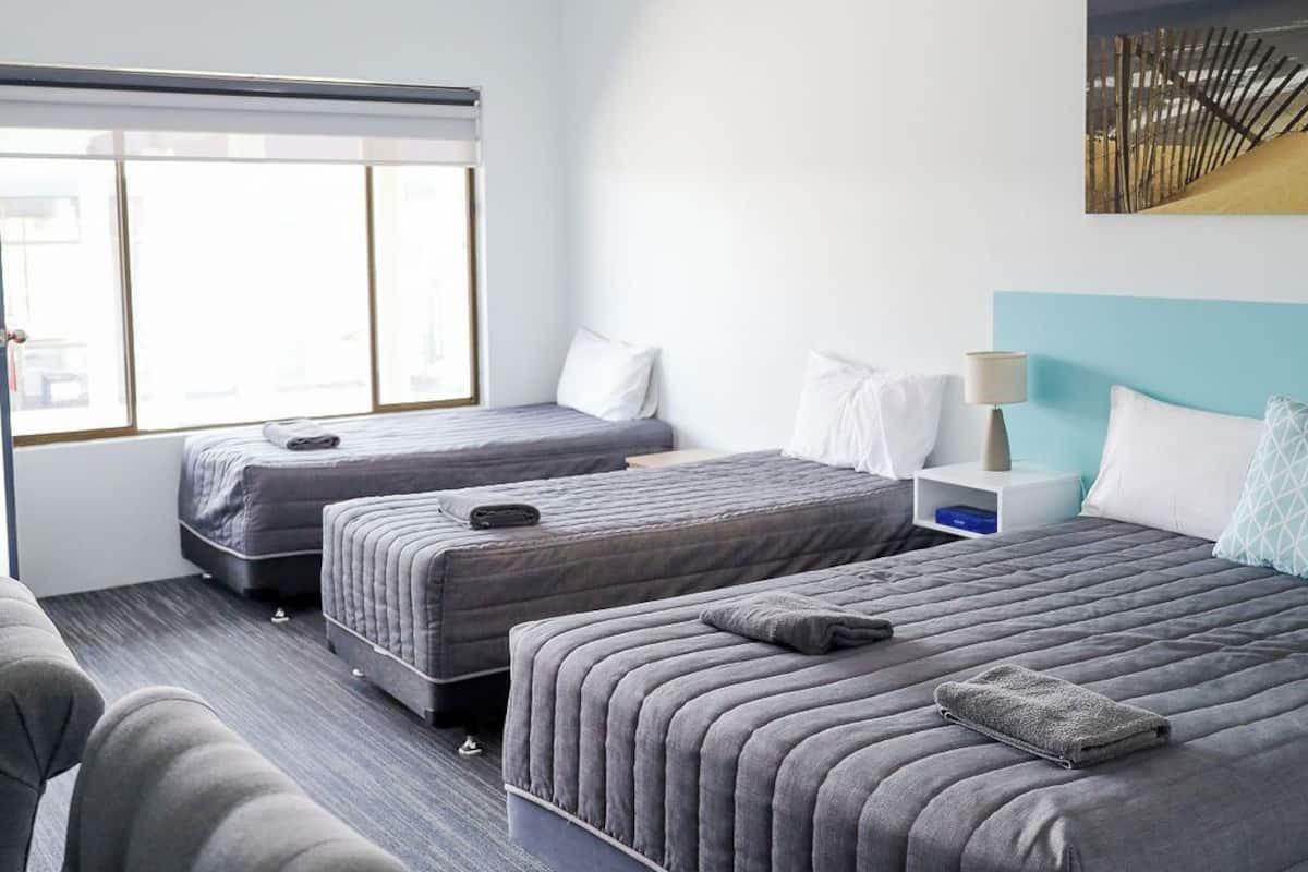 A hotel room with two beds, a sofa, a window, and a painting on the wall.
