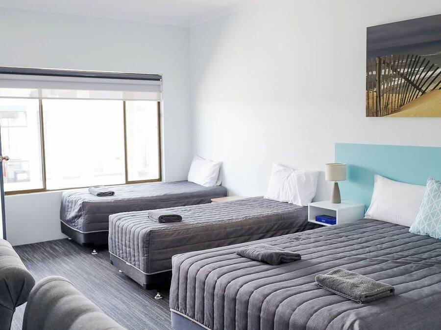 Quarto de hotel com duas camas, um sofá, uma janela e um quadro na parede.
