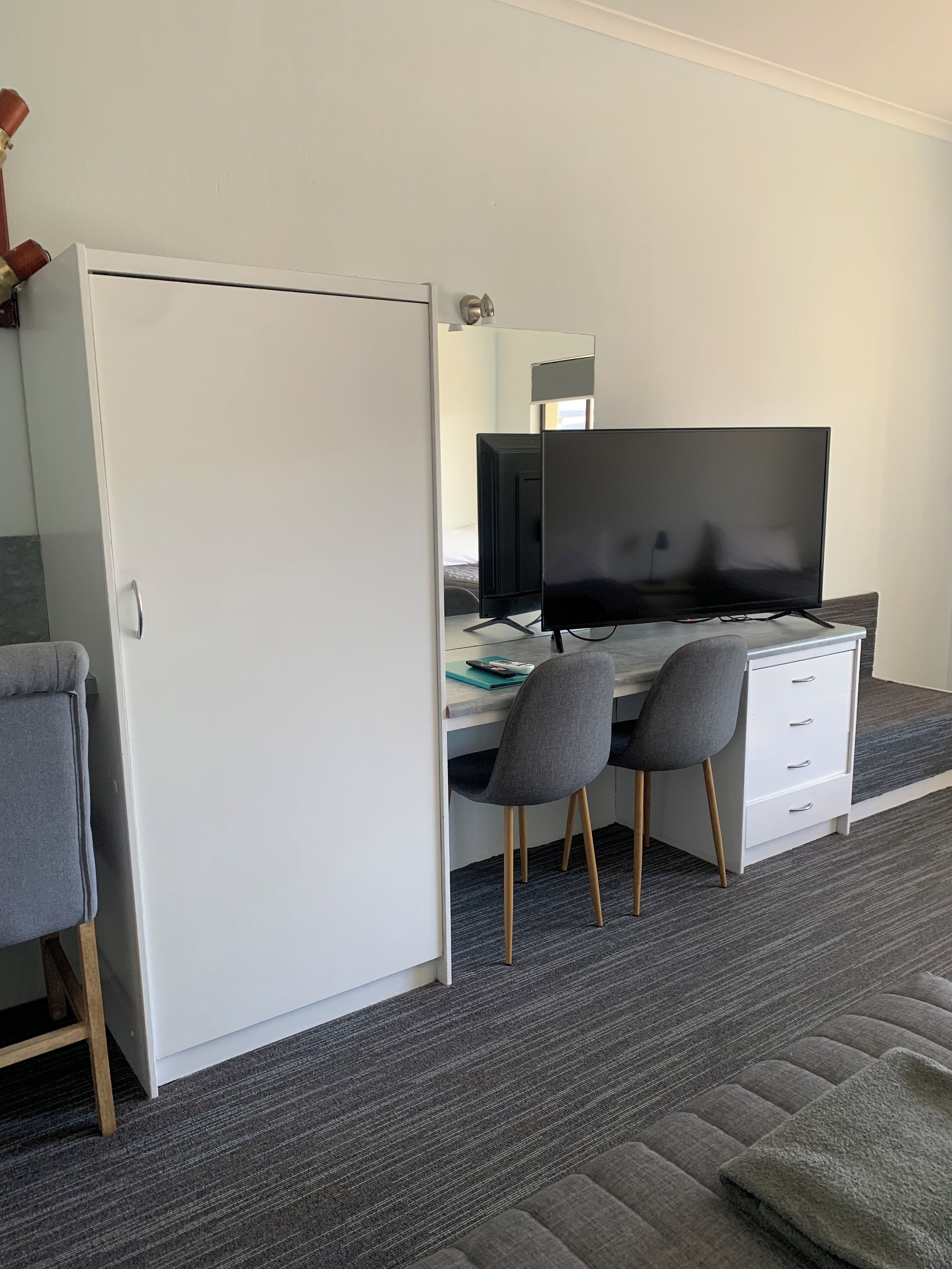 Una habitación moderna con escritorio, dos sillas, televisión de pantalla plana y armario.