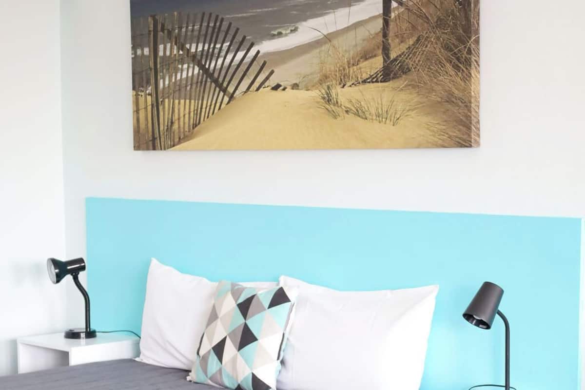 A hotel room with a bed, two bedside tables, a lamp, and a painting on the wall.