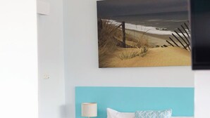 A modern hotel room with a bed, a nightstand, a lamp, and a painting of a beach scene.