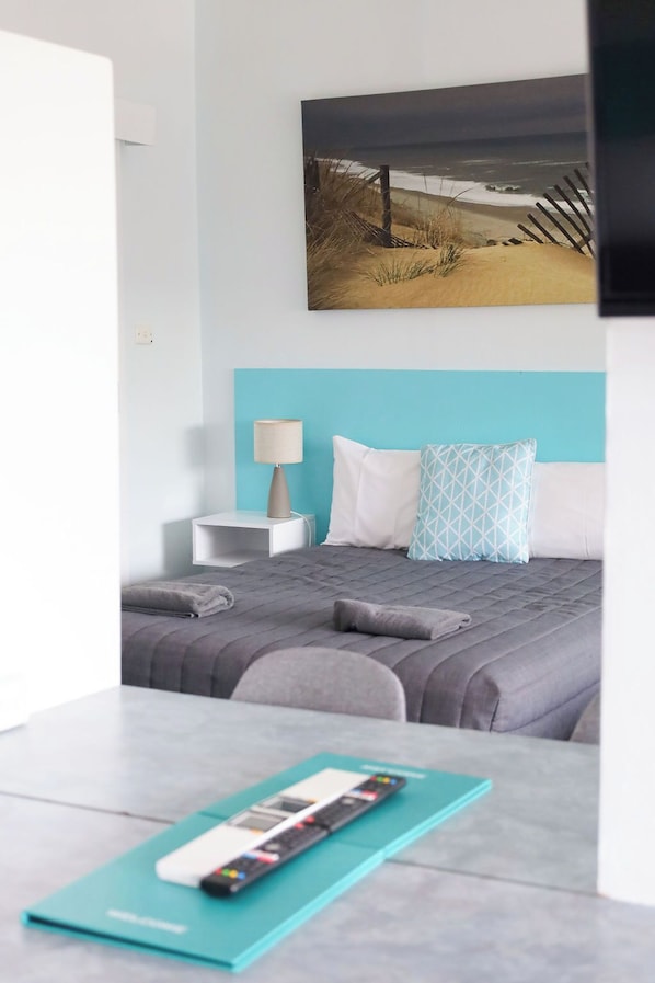 A modern hotel room with a bed, a nightstand, a lamp, and a painting of a beach scene. - Robetown Motor Inn & Apartments (Robe)
